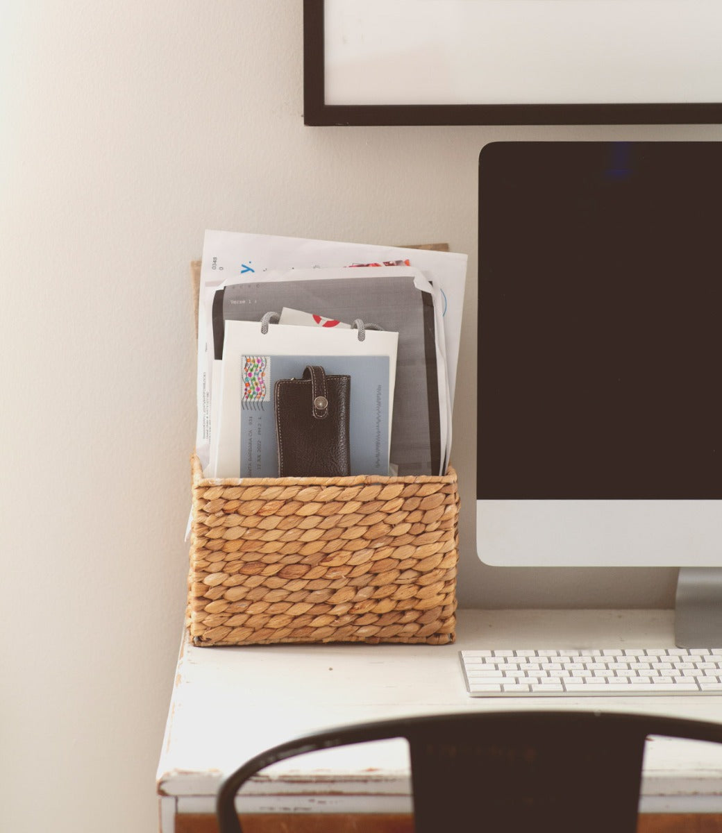 A Behold wicker basket on a desk next to a computer.