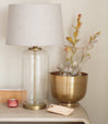 A Behold glass vase with a plant and a lamp on a table. (Brand: Bed Stu)