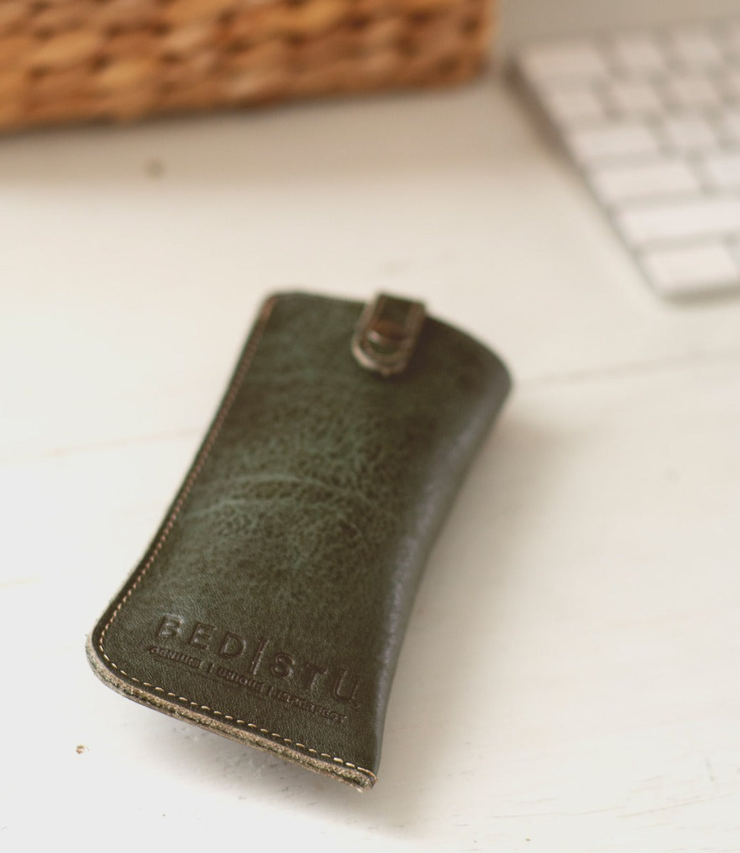 A green leather Behold eyeglass case on a table next to a keyboard. (Brand: Bed Stu)