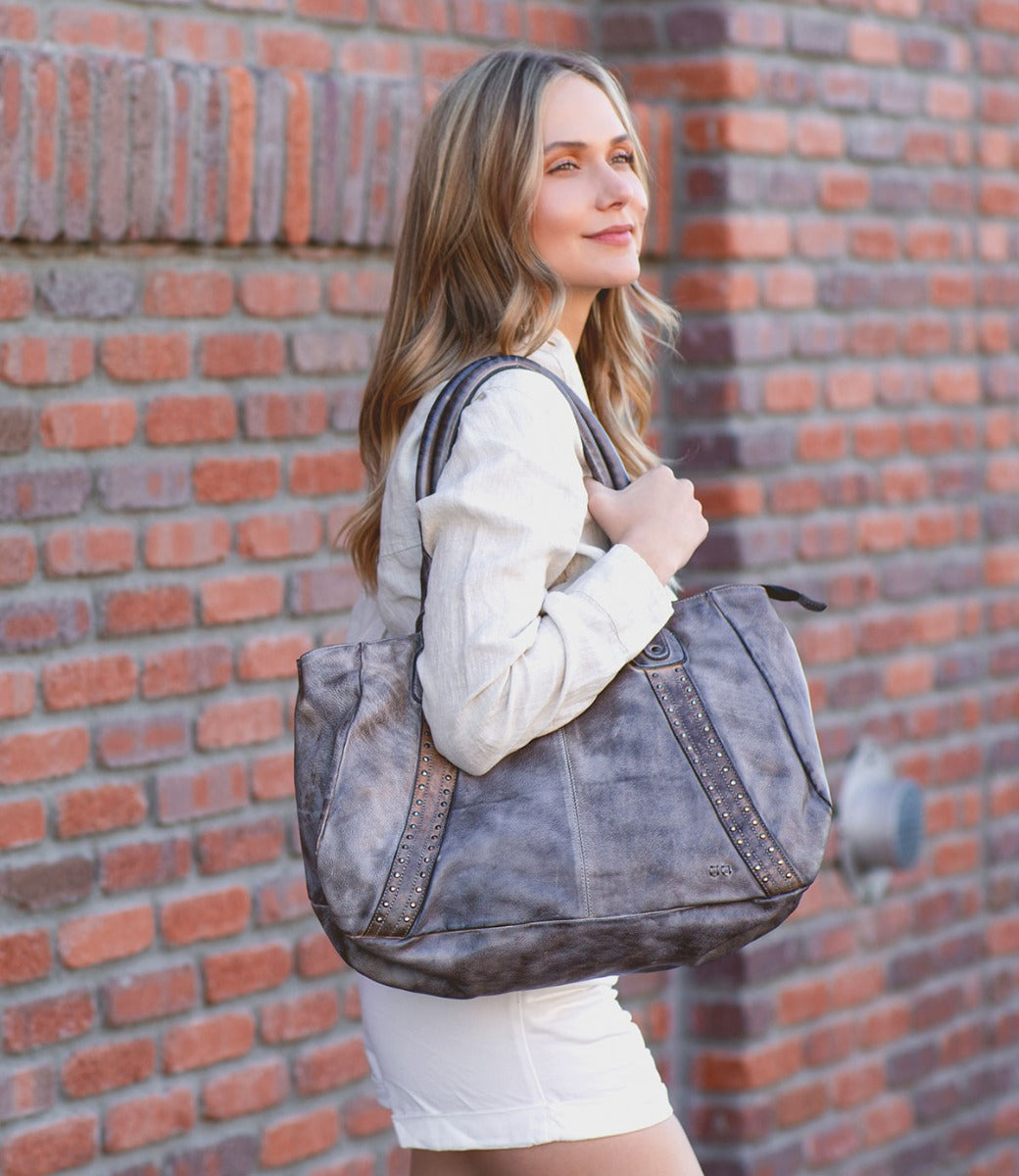 A woman in white shorts is holding a Bed Stu Geraldin tote bag.