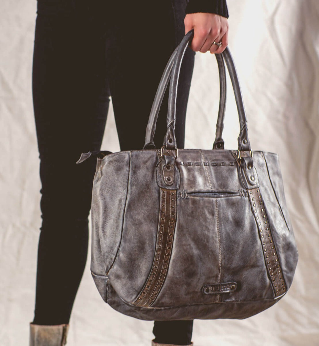 A woman is holding a grey leather Bed Stu Geraldin tote bag.