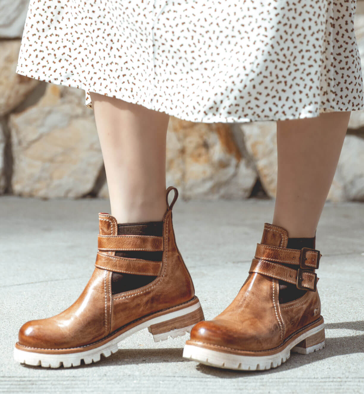 A woman wearing Bed Stu Ginger brown leather ankle boots and a polka dot dress.