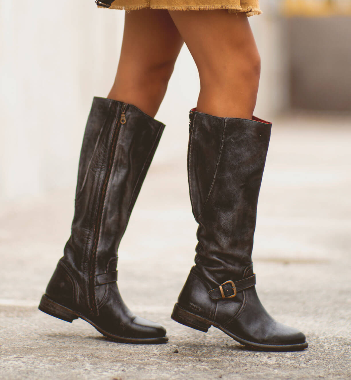 A woman wearing black Glaye riding boots and a yellow skirt. (Product Name: Glaye, Brand Name: Bed Stu)