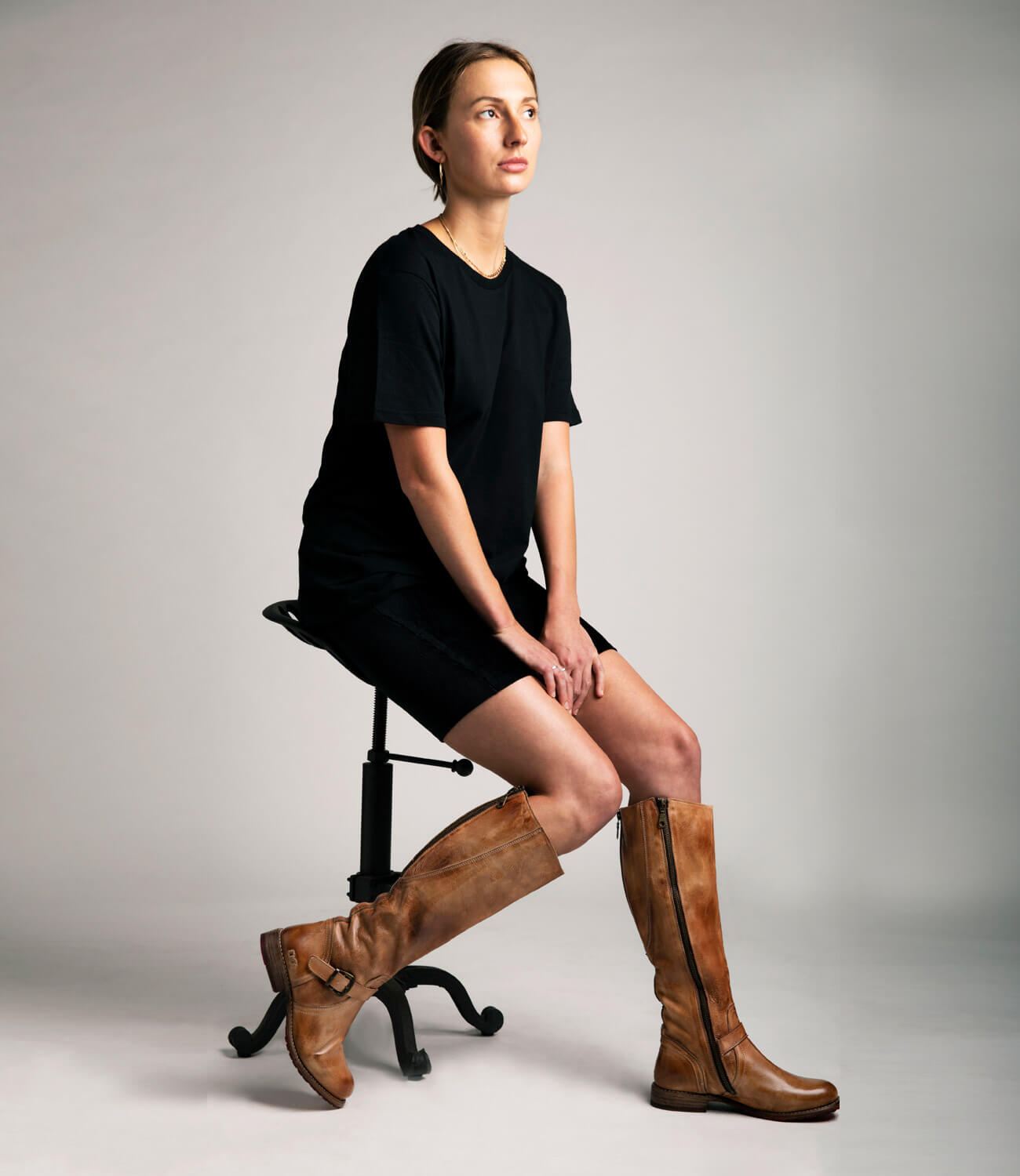 A woman sitting on a stool in a pair of Bed Stu Glaye boots.