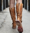 A woman is walking down a street in a pair of Bed Stu Glaye boots.