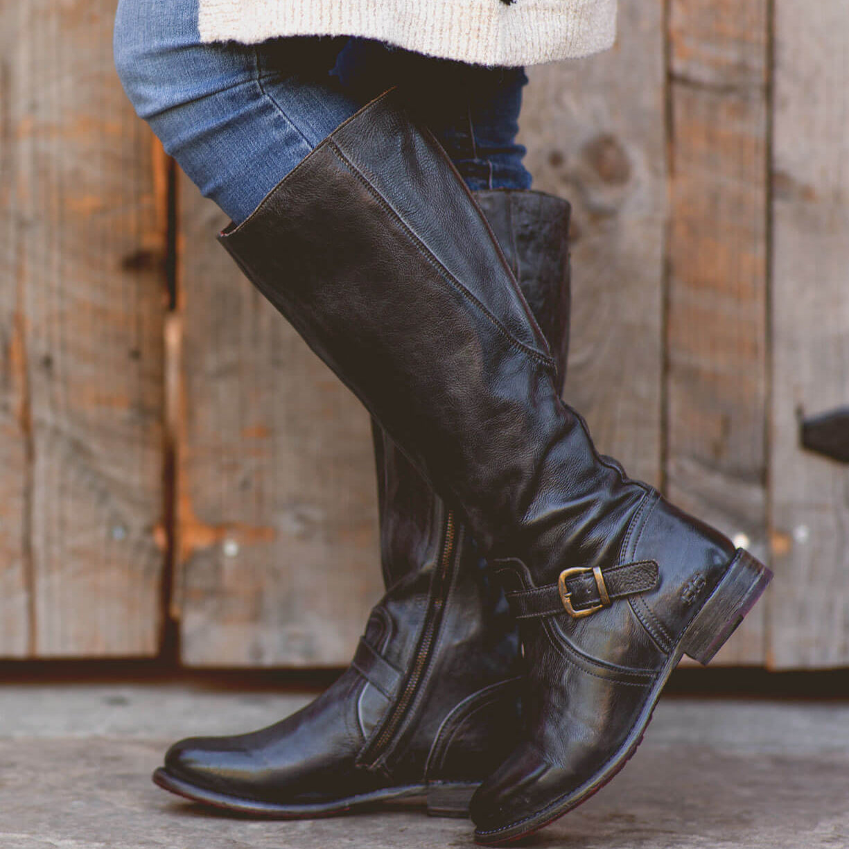 A woman wearing Glaye wide calf black boots by Bed Stu and a sweater.
