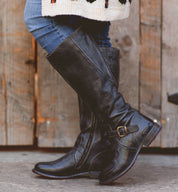 A woman wearing Glaye wide calf black boots by Bed Stu and a sweater.
