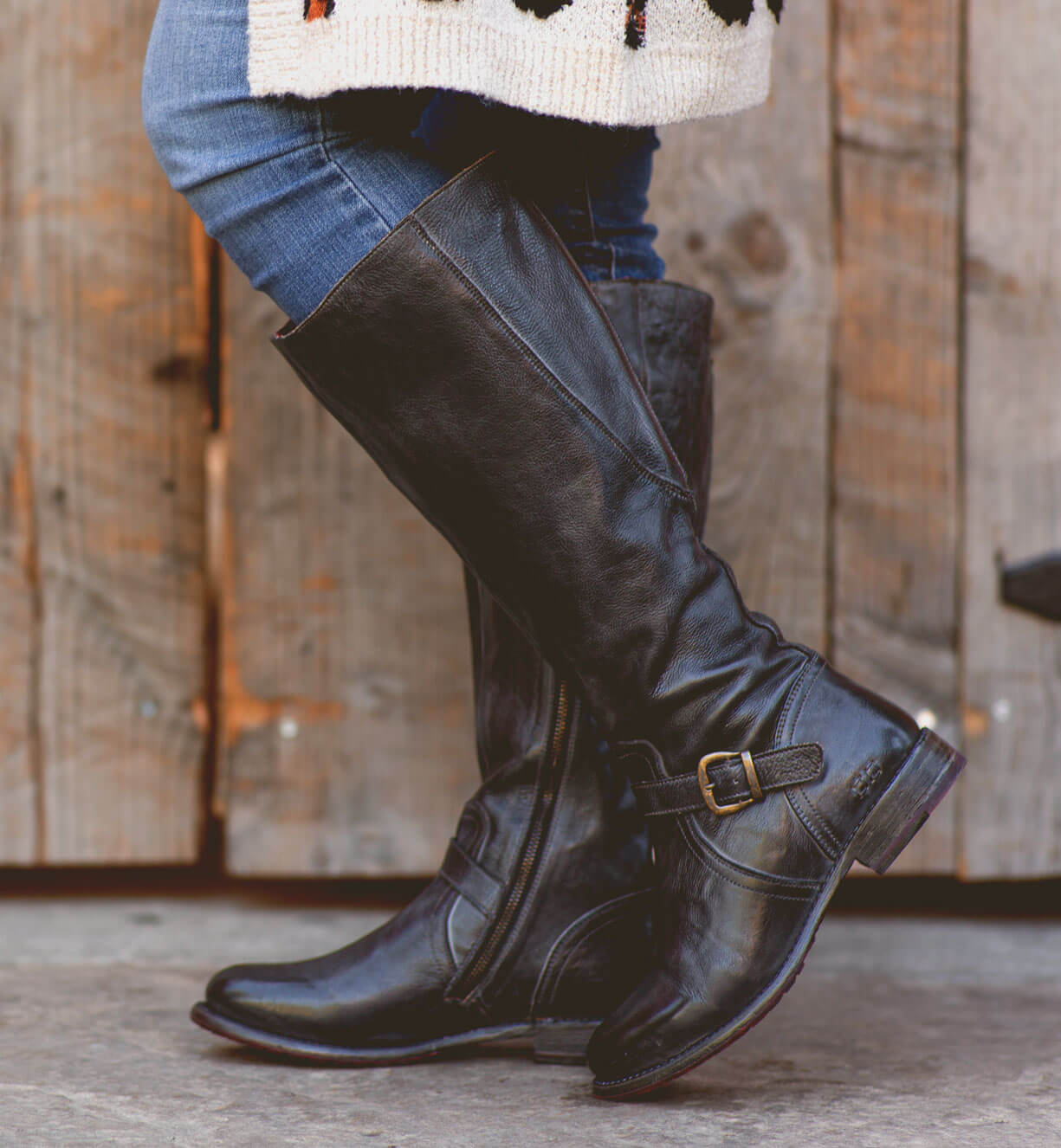 A woman wearing Glaye wide calf black boots by Bed Stu and a sweater.