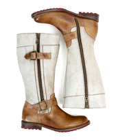 A pair of "Gogo Lug" mid-calf leather boots by Bed Stu with brown leather soles, light beige shafts, and decorative buckles. The boots feature dual zippers for easy wear and a durable lug outsole for added traction.