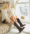 A woman sitting on a couch with a pair of Bed Stu Gogo Lug boots.