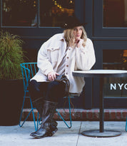 A woman sitting at an outdoor table wearing a hat and Bed Stu Gogo Lug Wide Calf boots.