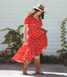 A woman wearing a red floral dress and Bed Stu cowboy boots.
