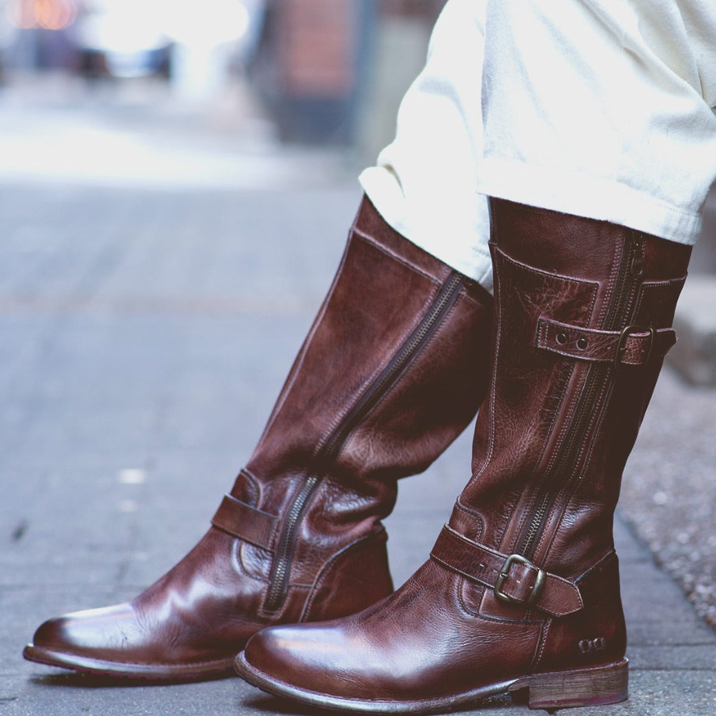 A person wearing Bed Stu Gogo Lug Wide Calf boots on a sidewalk.