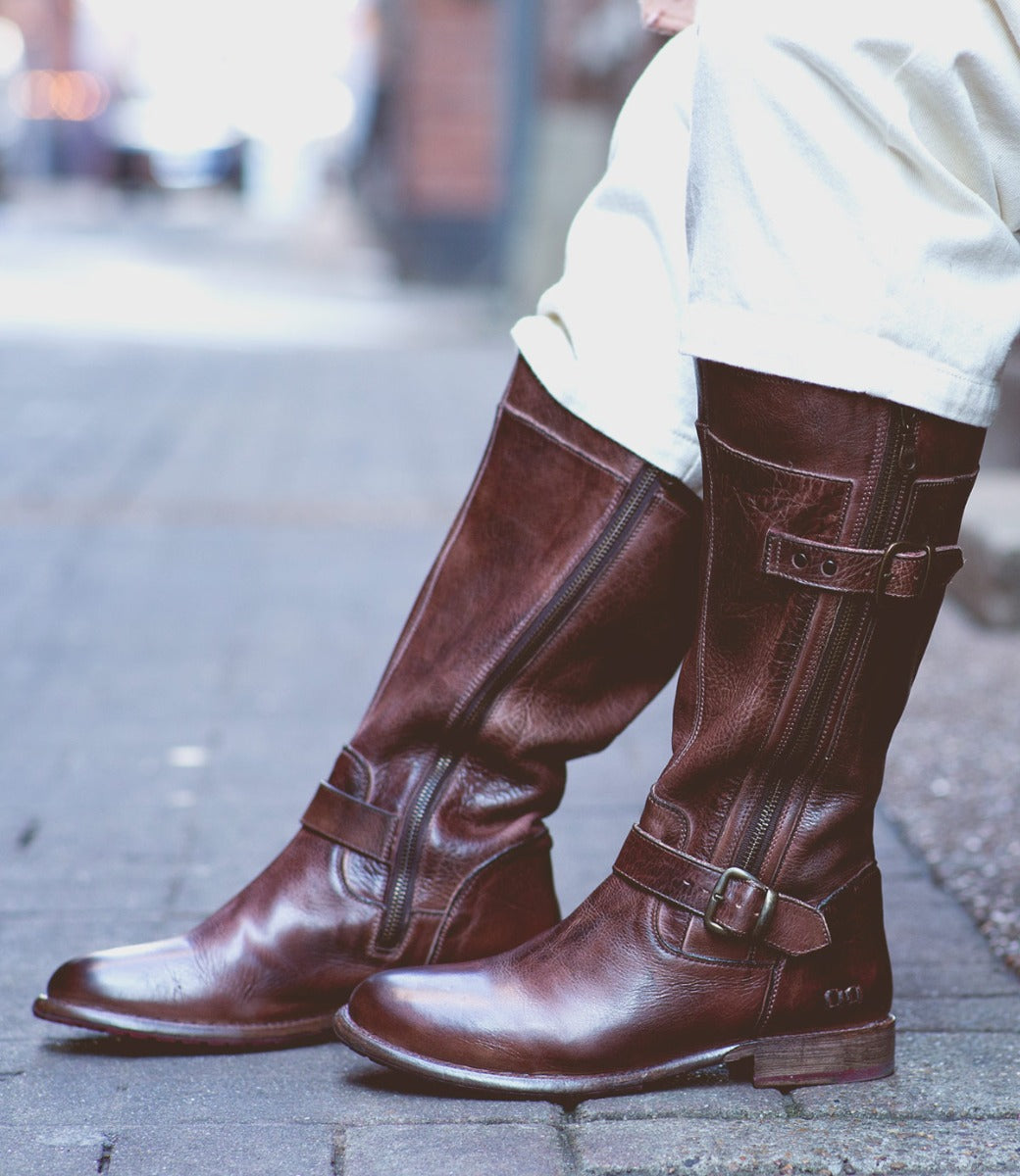 A person wearing Bed Stu Gogo Lug Wide Calf boots on a sidewalk.