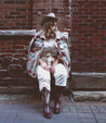A woman in a Bed Stu cowboy hat and Bed Stu cowboy boots sitting on a brick wall.
