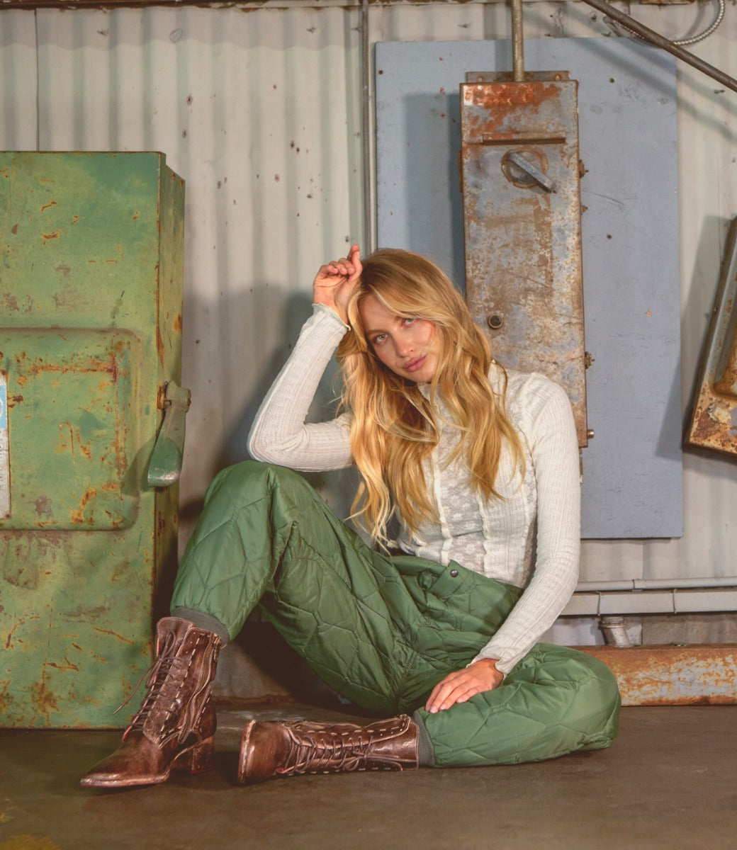 A woman sitting on the ground in pants and Gracie Bed Stu boots.