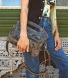 A woman in Bed Stu jeans and a Bed Stu tee shirt holding a Greenway purse.