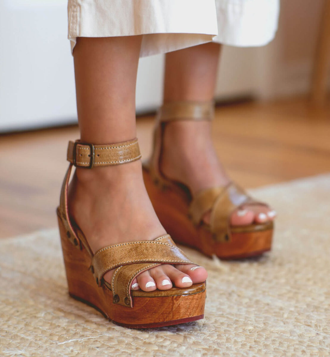 A woman's feet standing on a rug in a pair of Bed Stu Grettell sandals.