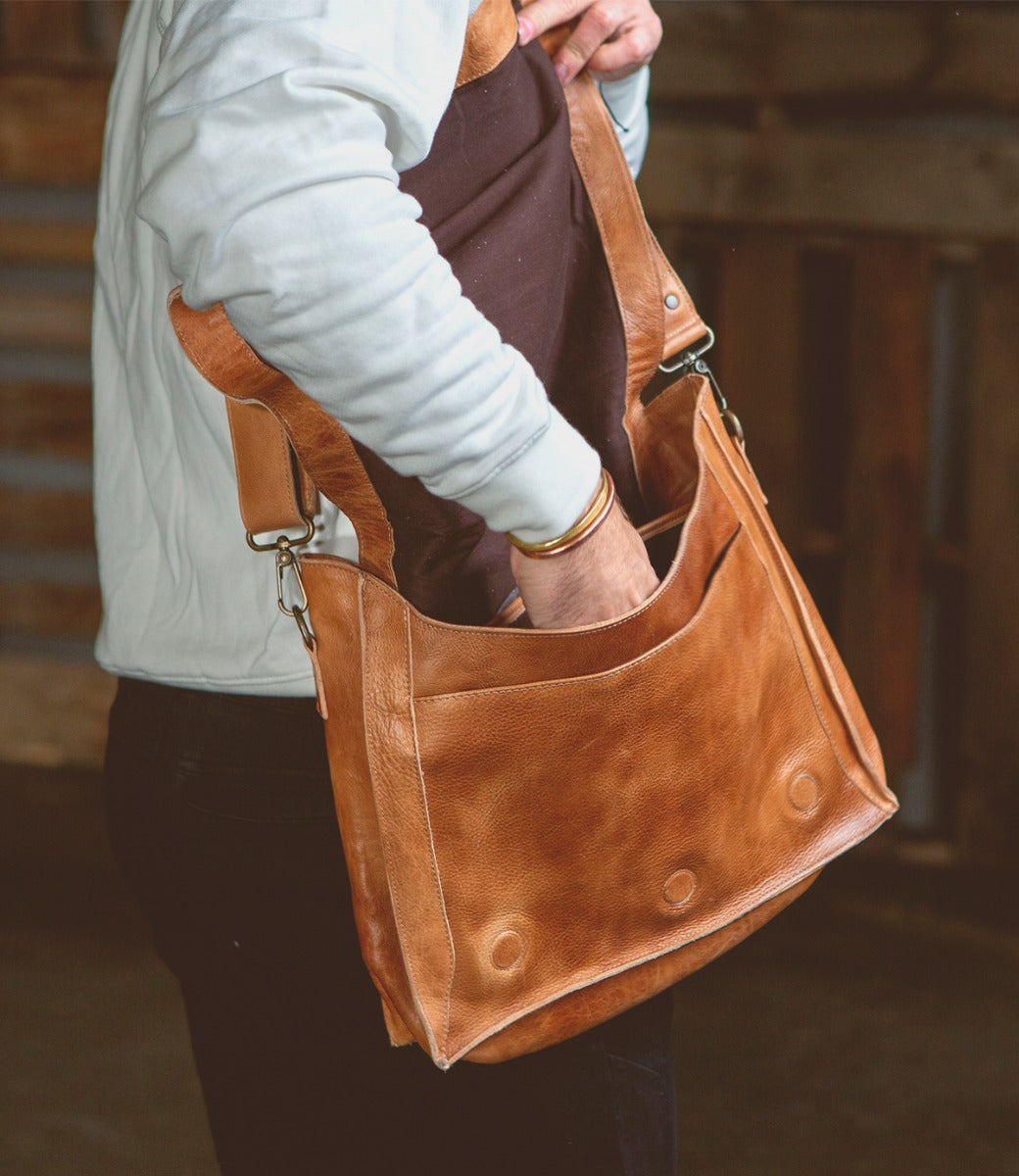 A man is holding a Bed Stu Hampton II tan leather bag.