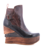 The Bed Stu Harmonious is a brown and black platform wedge ankle boot with a buckle, thick sculptural wood wedge sole, and bold red leather interior.