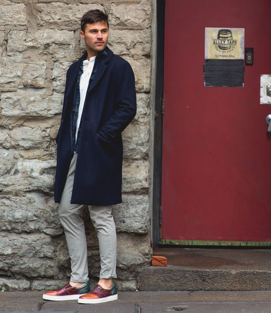 A man wearing a Harry coat leaning against a door.