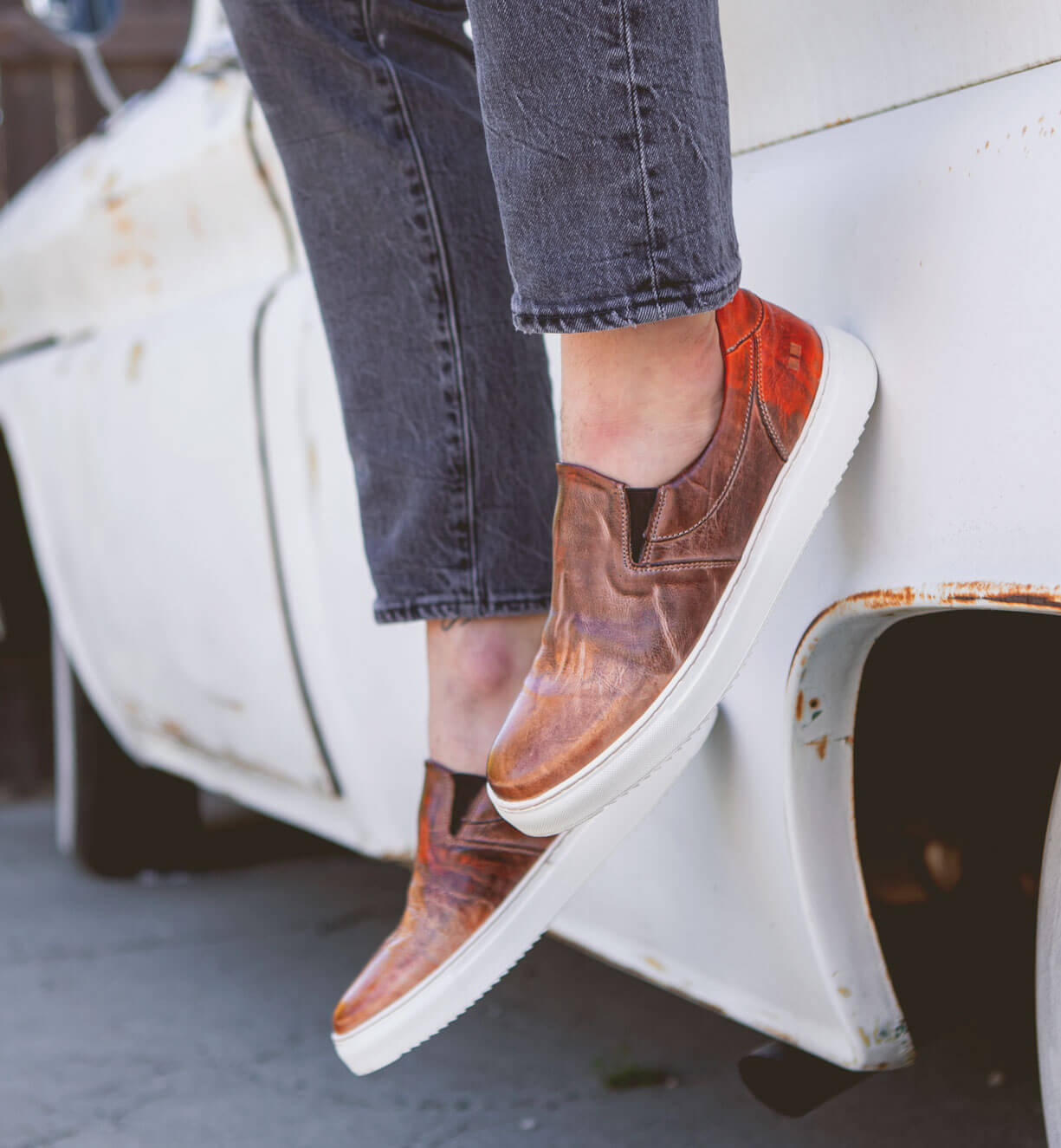 A person standing on the side of a truck wearing a pair of Harry slip on sneakers from Bed Stu.