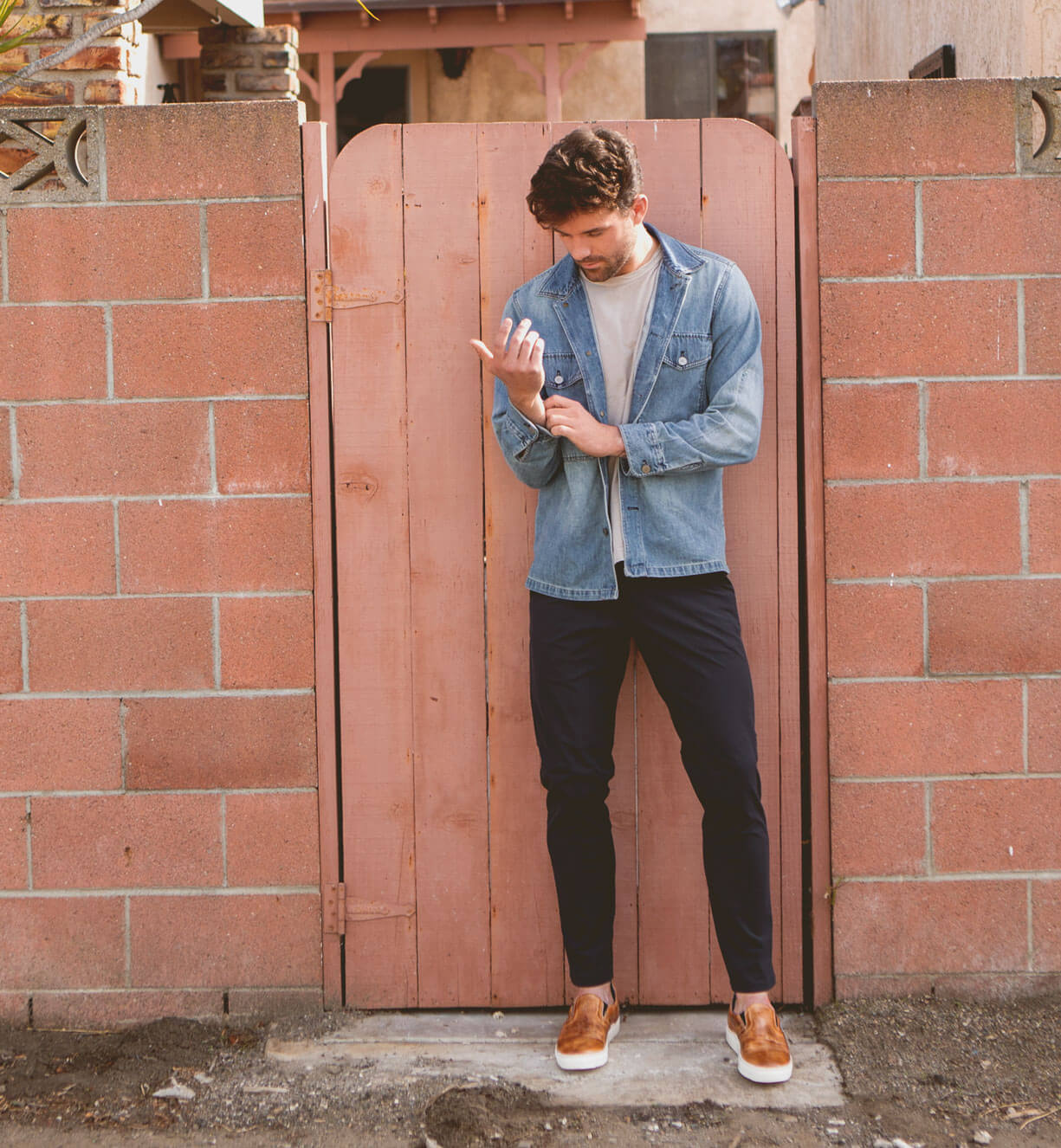 A man leaning against a brick wall holding a Bed Stu cell phone named Harry.