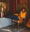 A man sitting in a chair next to a Bed Stu Harry acoustic guitar.