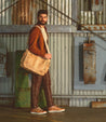 A man is holding a Bed Stu Hawkeye II tan leather messenger bag.