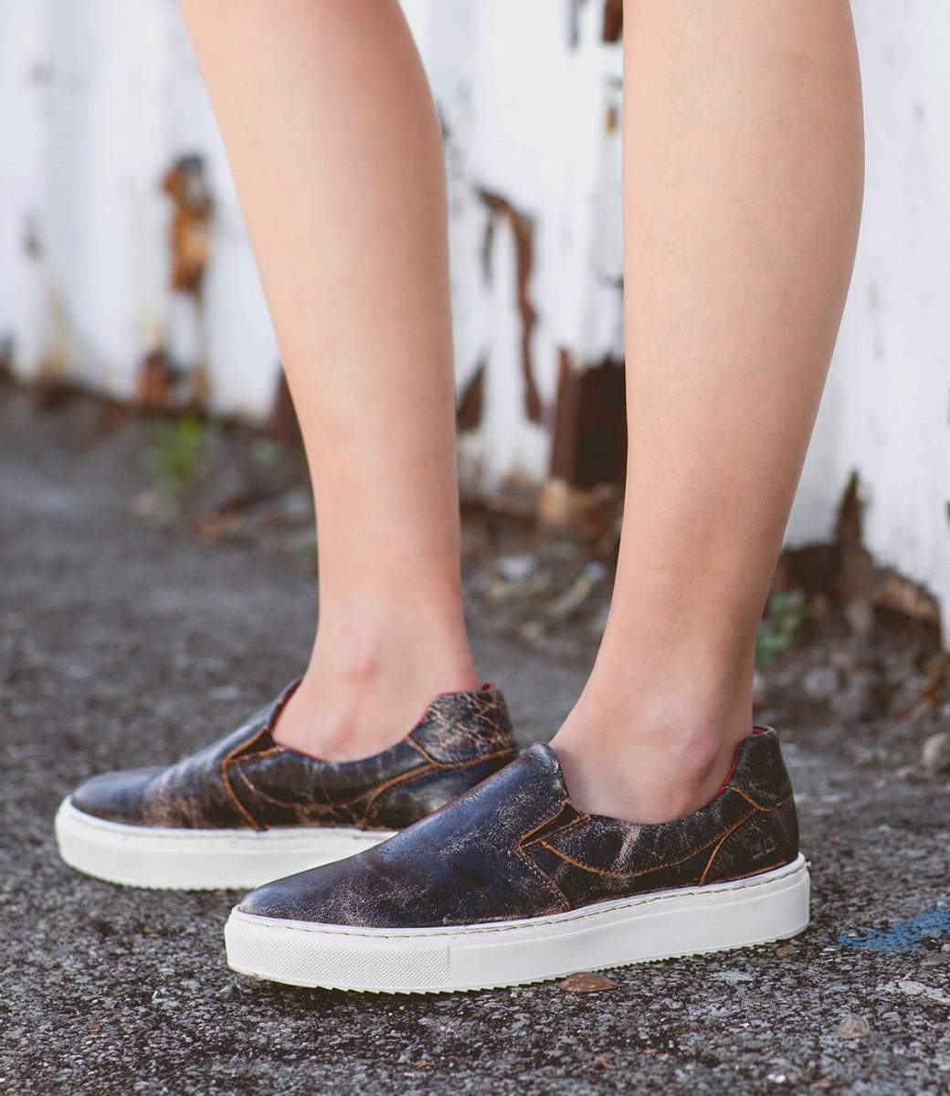A woman wearing a pair of brown Hermione slip on sneakers by Bed Stu.