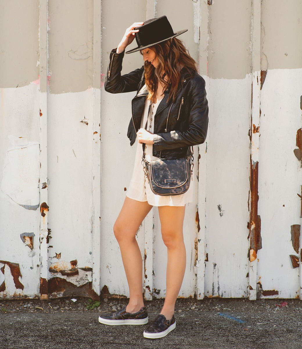 A woman in a Hermione hat and Bed Stu leather jacket standing next to a wall.