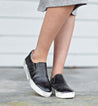 A woman wearing a pair of black Hermione slip on sneakers by Bed Stu.
