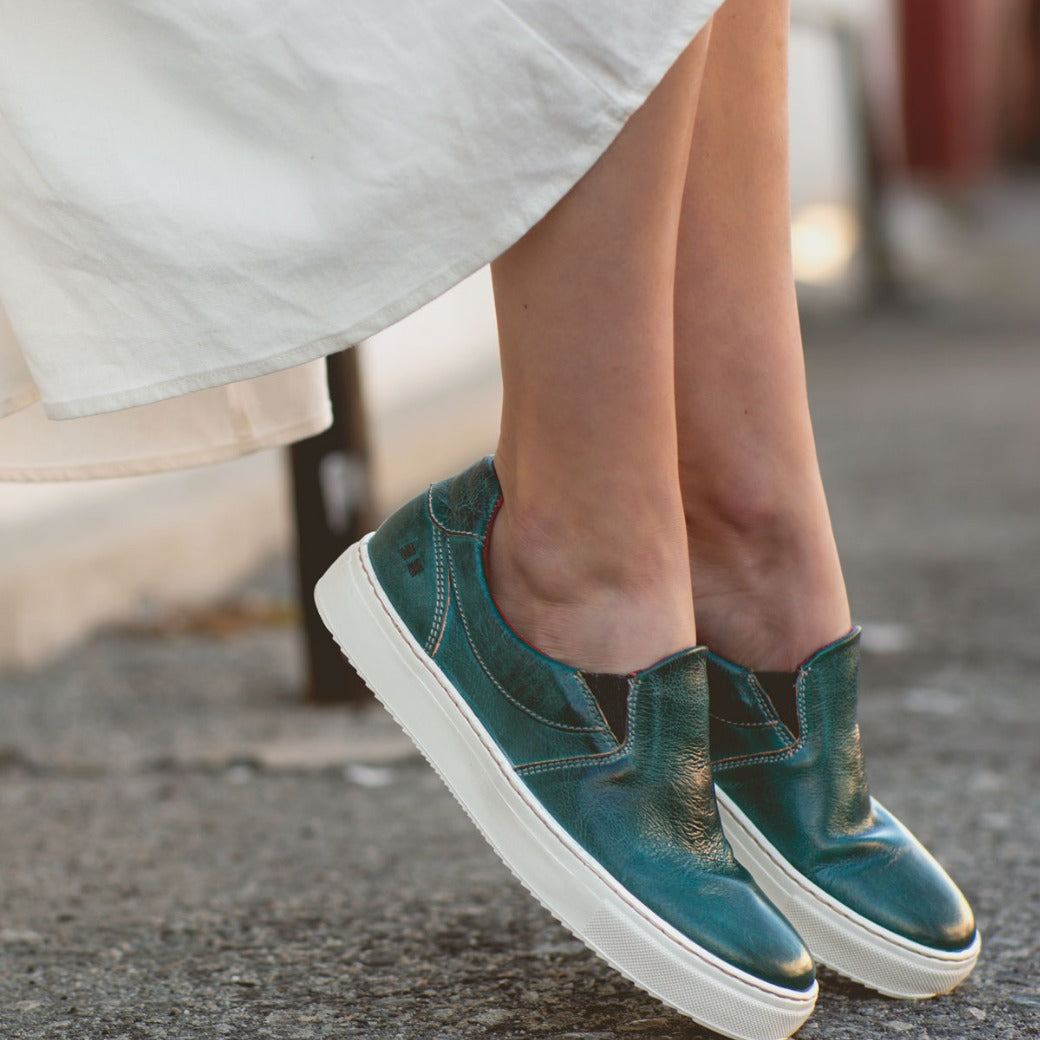A woman wearing a white dress and Bed Stu Hermione slip on sneakers.
