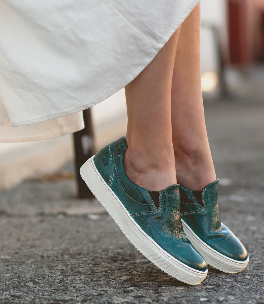 A woman wearing a white dress and Bed Stu Hermione slip on sneakers.