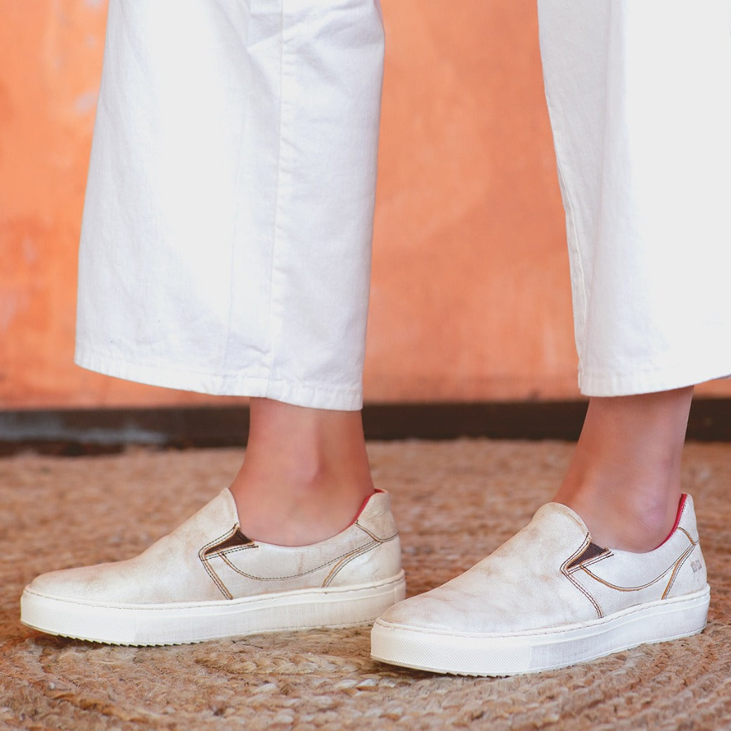 A woman wearing white pants and white Bed Stu Hermione slip on sneakers.