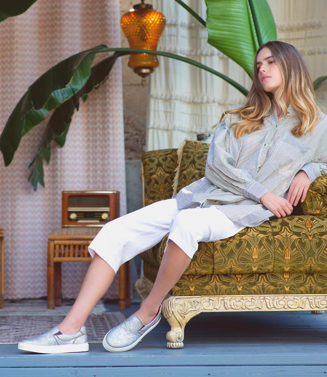 A woman is sitting on a Hermione couch in front of a plant.