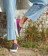 A woman wearing Hermione jeans and Bed Stu sneakers leaning against a brick wall.