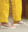 A person wearing Bed Stu yellow pants and Bed Stu white sandals.