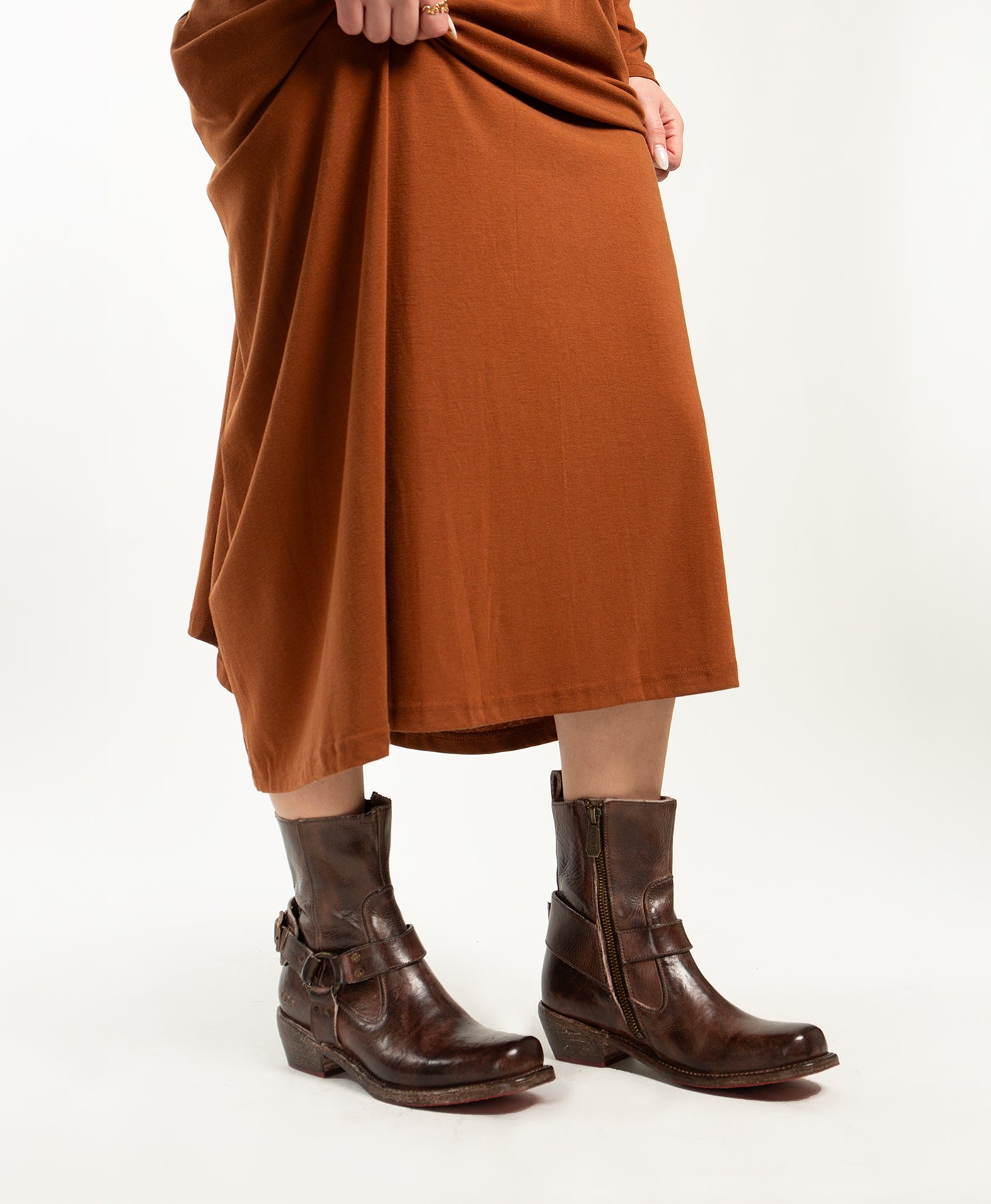 A person wearing the Homage rust-colored midi dress paired with Bed Stu dark brown square toe boots with buckles, standing against a plain white background.
