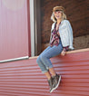 A woman wearing Honor jeans and a Bed Stu denim jacket sitting on the ledge of a barn.