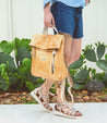 A woman wearing denim shorts and sandals holding a Bed Stu Howie backpack.