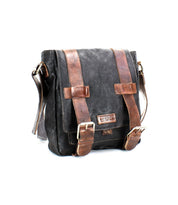 Presenting the Hue by Bed Stu, a versatile black leather satchel standing against a plain white background, distinguished by its brown straps and brass buckles. It also features an adjustable strap for added convenience.