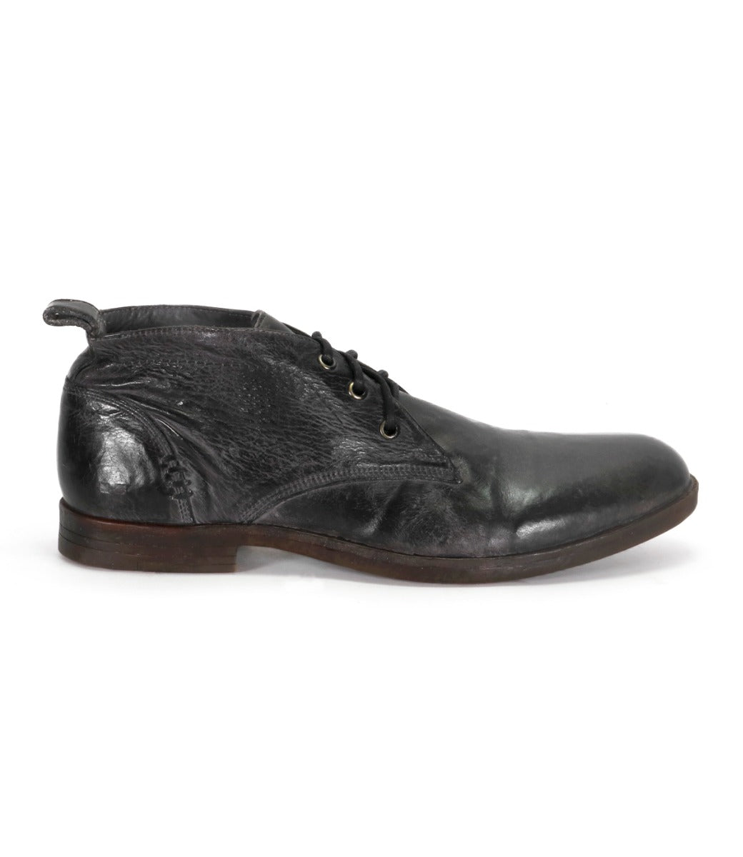 The Bed|Stü Illiad, a black leather chukka dress shoe with a modern lace-up design and a slightly worn appearance, is displayed in a left side view against a white background.