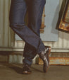 A man in jeans and a pair of Bed Stu Illiad boots leaning against a wall.