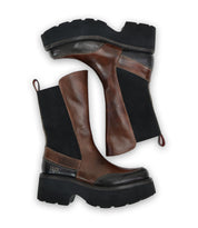 A pair of Bed Stu's Illicit platform boots, featuring brown leather and black fabric with chunky soles and a nostalgic fashion vibe, positioned sideways against a white background.