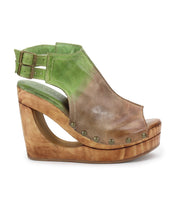 The Imelda by Bed Stu is a green and brown open-toe wedge sandal featuring a wood-effect platform, distinctive cutout heel, ankle strap, and rivet details.