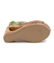 The image showcases the Imelda sandal by Bed Stu, featuring a wooden platform sole with a green strap and buckle. It has a unique cutout that adds flair to its stylish open-toe design.