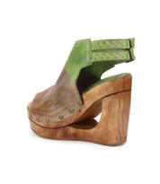 Side view of Bed Stu's Imelda sandal, a high wooden wedge with open-toe design, featuring green and brown leather upper, cutout heel, and metal stud accents.