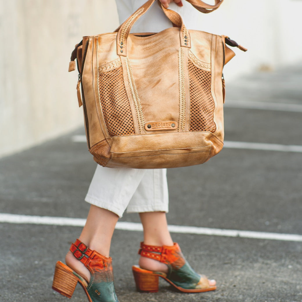 A woman carrying a tan tote bag wearing Ireni shoes by Bed Stu.