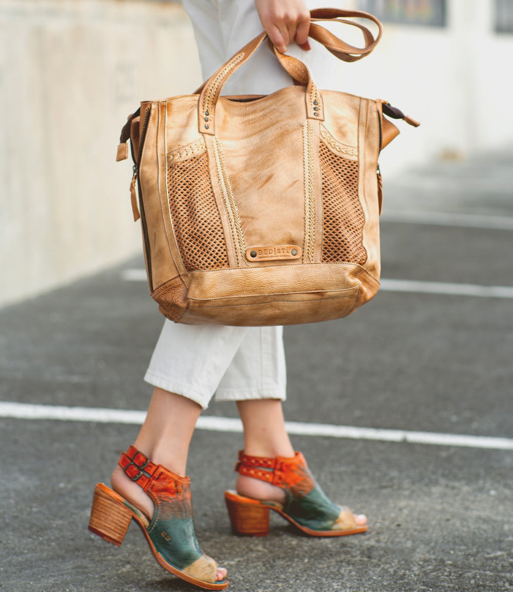 A woman carrying a tan tote bag wearing Ireni shoes by Bed Stu.